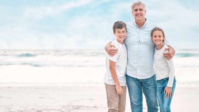 A 60-year-old father embraces his son and daughter during a walk on the beach.