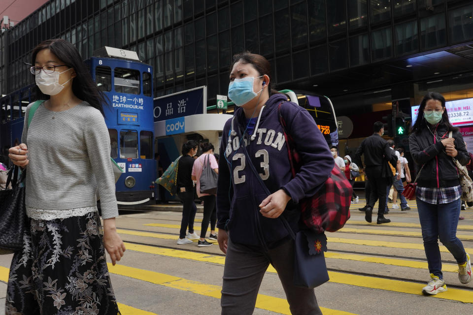 People wearing face masks walk at a down town street in Hong Kong Wednesday, March 25, 2020. For most, the coronavirus causes only mild or moderate symptoms, such as fever and cough. But for a few, especially older adults and people with existing health problems, it can cause more severe illnesses, including pneumonia. (AP Photo/Vincent Yu)