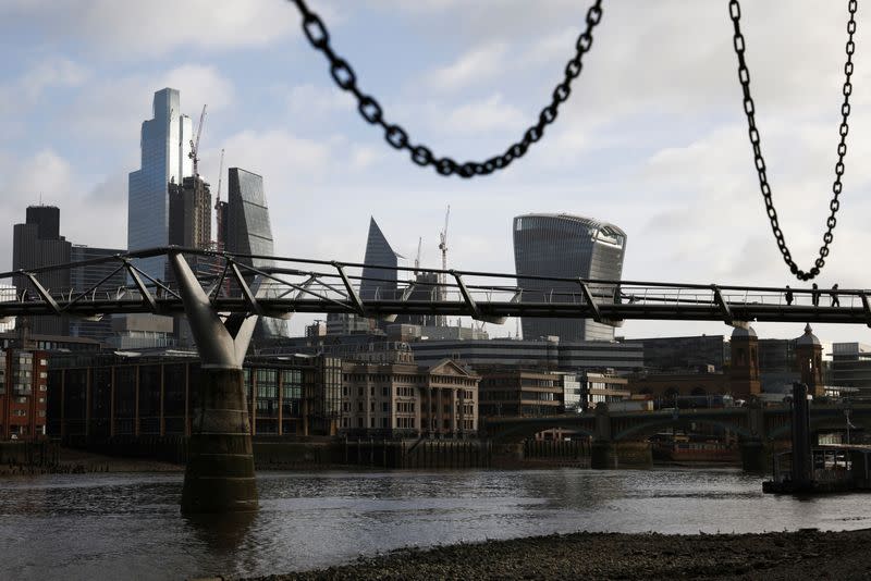 FILE PHOTO: The City of London financial district is seen as people walk over Millennium Bridge in London