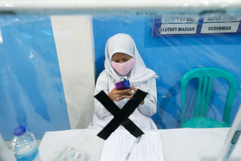 A student wearing a protective face mask checks their mobile phone at a community hall offering free WiFi access provided by the government for online schooling in Jakarta