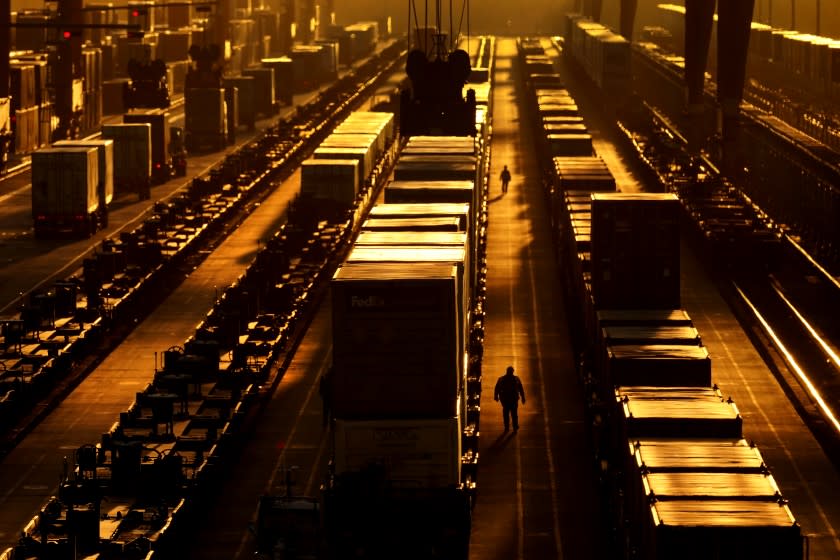 Workers walk along the tracks at an intermodal facility as the sun sets Monday, Dec. 21, 2020, in Edgerton, Kan. The facility, operated by BNSF railway, transfers shipping containers between rail cars to trucks. (AP Photo/Charlie Riedel)