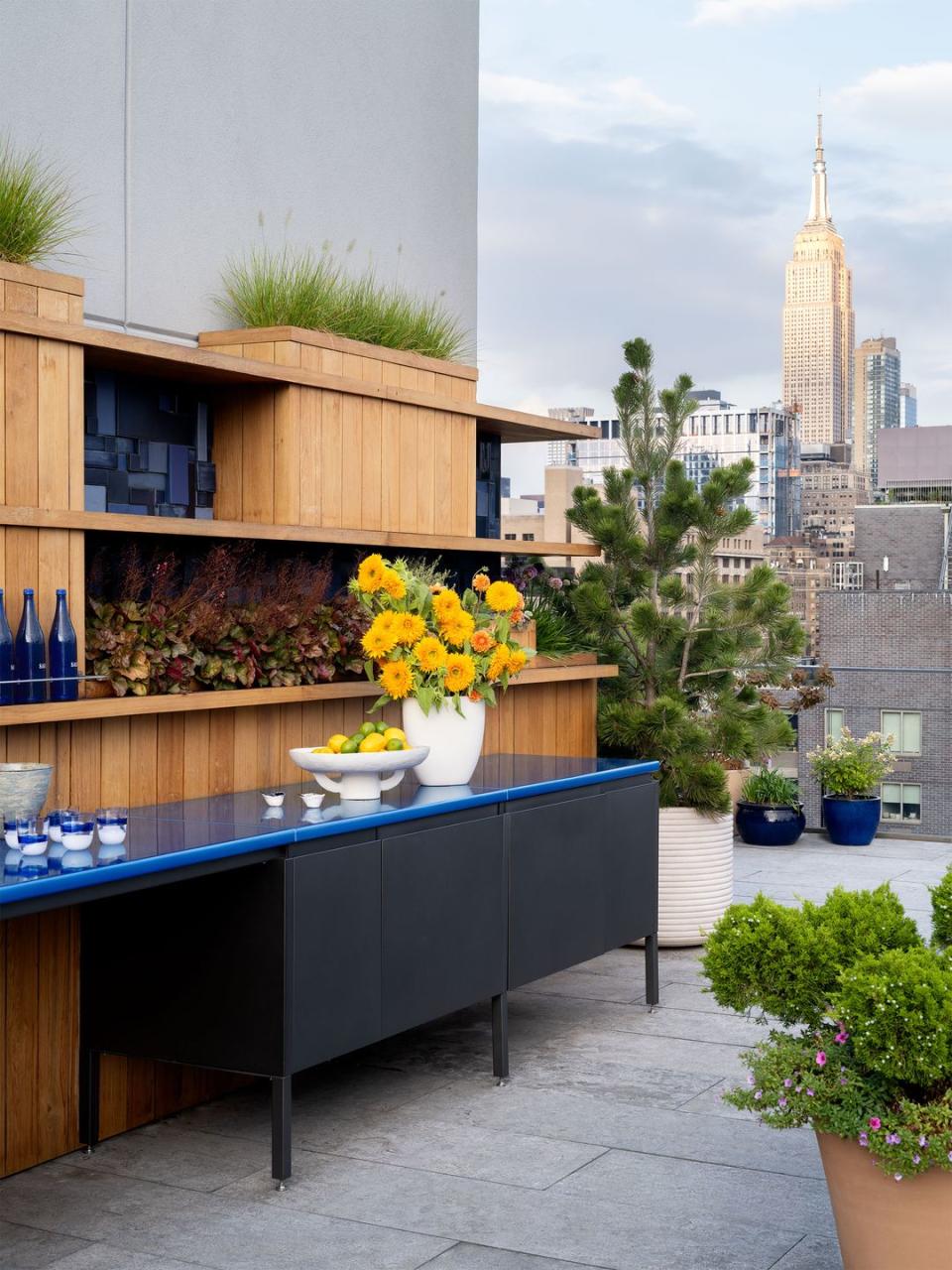 outdoor kitchen counter in blue with yellow flowers in a white vase atop it and the manhattan skyline in the background