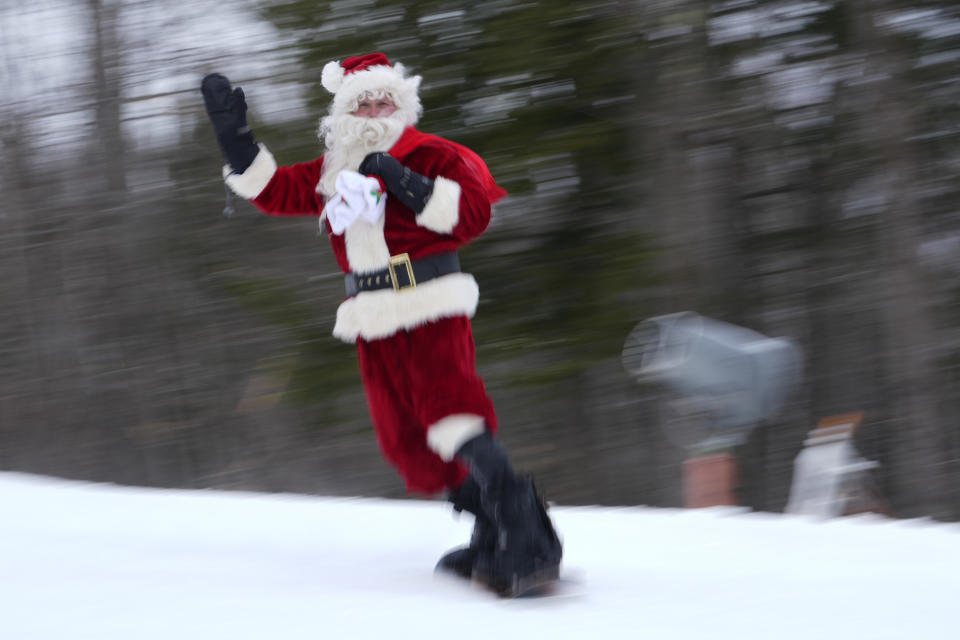 A snowboarder dressed as Santa waves while hitting the slopes.