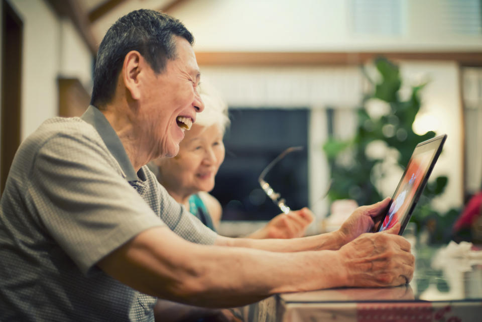 Senior couple look at photos on tablet happily