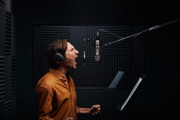 A man shouts into a microphone in a studio booth.