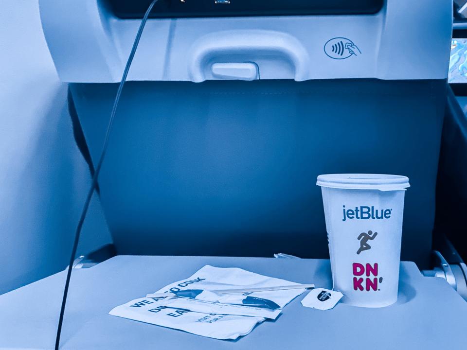 A white to-go coffee cup on the right side of a gray tray table on a flight