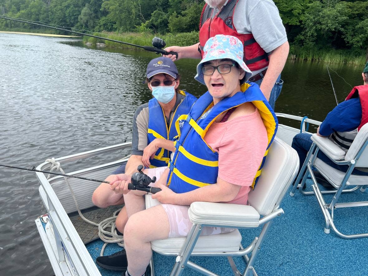 Tracey Donovan, a resident with one of the Ottawa-Carleton Association for Persons with Developmental Disabilities' homes, gets fishing assistance from the group's recreation counsellor Wayne Hughes. On their August outing, Donovan caught and released a 20-centimetre perch.  (Giacomo Panico/CBC - image credit)