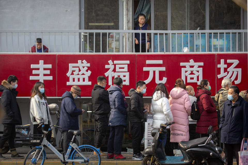 A woman looks at at people lined up for mass COVID-19 testing in a central district of Beijing, Friday, Jan. 22, 2021. Beijing has ordered fresh rounds of coronavirus testing for about 2 million people in the downtown area following new cases in the Chinese capital. (AP Photo/Mark Schiefelbein)