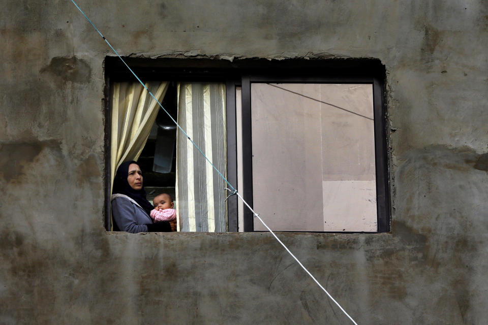 In this Tuesday, Dec. 18, 2018, photo, a Syrian refugee looks through a window as she holds her daughter in Ouzai refugee compound, in the southern port city of Sidon, Lebanon. A much touted Russian initiative to facilitate the return of Syrian refugees has fizzled out, with the return of only about 114,000 Syrians - out of more than 5 million in the region and Europe. In Lebanon, which hosts the highest ratio of refugees per capita, most of the estimated 1.2 million Syrians say the intend to stay put, citing economic concerns, ongoing fighting and destroyed homes. (AP Photo/Bilal Hussein)