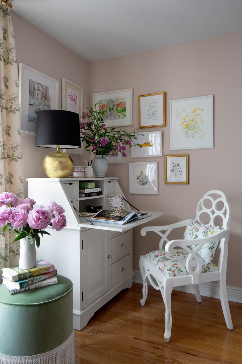 Corner gallery wall, fold down white secretary desk, purple floral arrangement, black lamp shade on round gold base