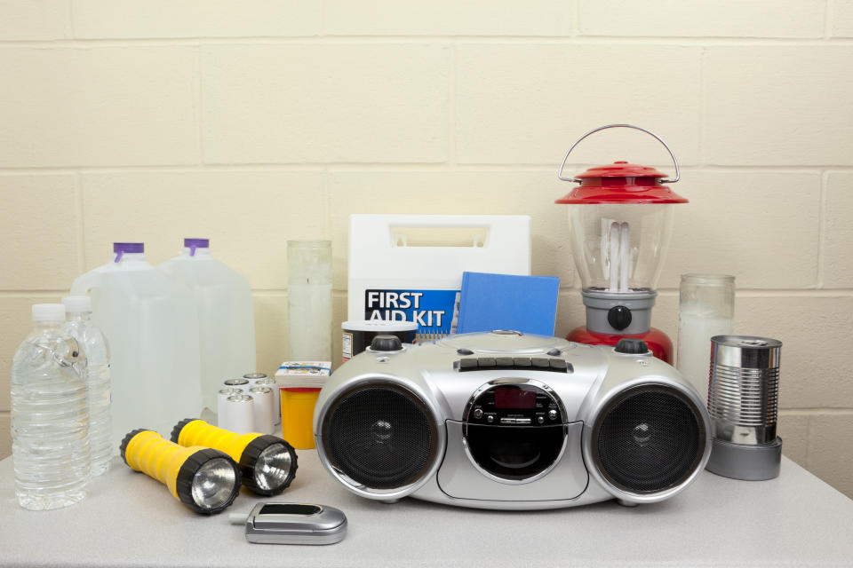 Emergency supplies on a table, including water, flashlight, radio, batteries, lantern, canned food, and a first aid kit