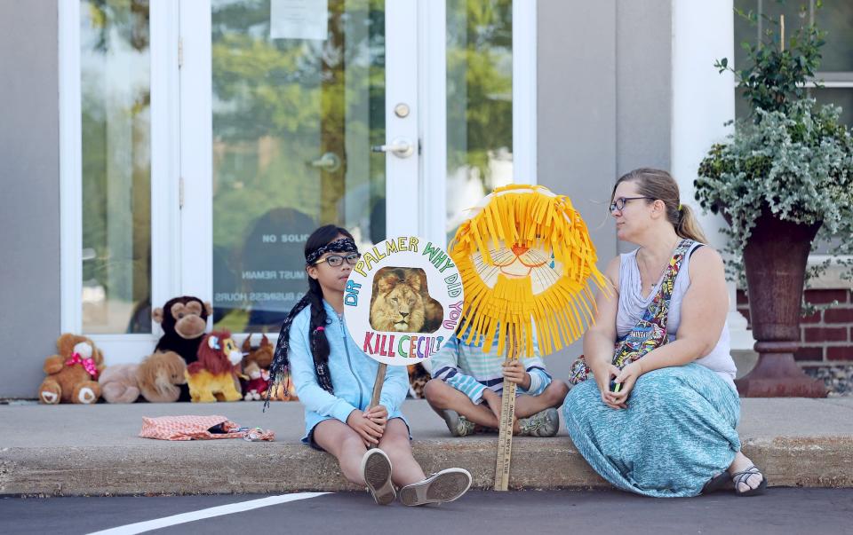 Hayley Hoppe (R) sits with her daughters Piper, 10, (L) and Paisley, 8, (C), in front of the doorway of River Bluff Dental clinic in protest against the killing of a famous lion in Zimbabwe, in Bloomington, Minnesota July 29, 2015. (REUTERS/Eric Miller)