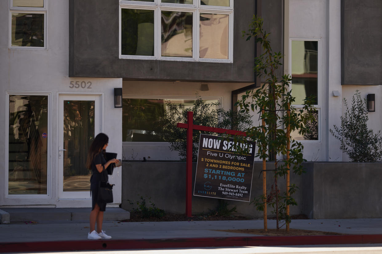 A woman stands near a 'for sale' sign displayed outside a townhouse style building in Los Angeles, California. The U.S. housing market is seeing a slow down in home sales due to the Federal Reserve raising mortgage interest rates to help fight inflation. (Credit: Allison Dinner/Getty Images)