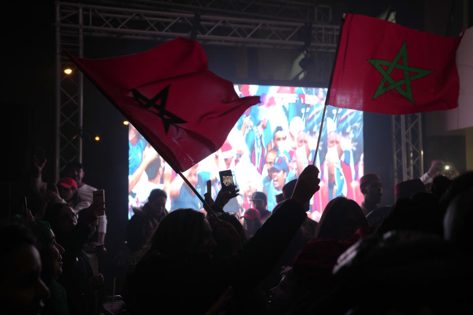 Moroccan fans wave flags as they stand in front of a screen after the end of the World Cup semifinal soccer match between France and Morocco that was being played in Qatar, in Rabat, Morocco, on Wednesday, Dec. 14, 2022. France won the Morocco 2-0. (AP Photo/Ben Curtis)