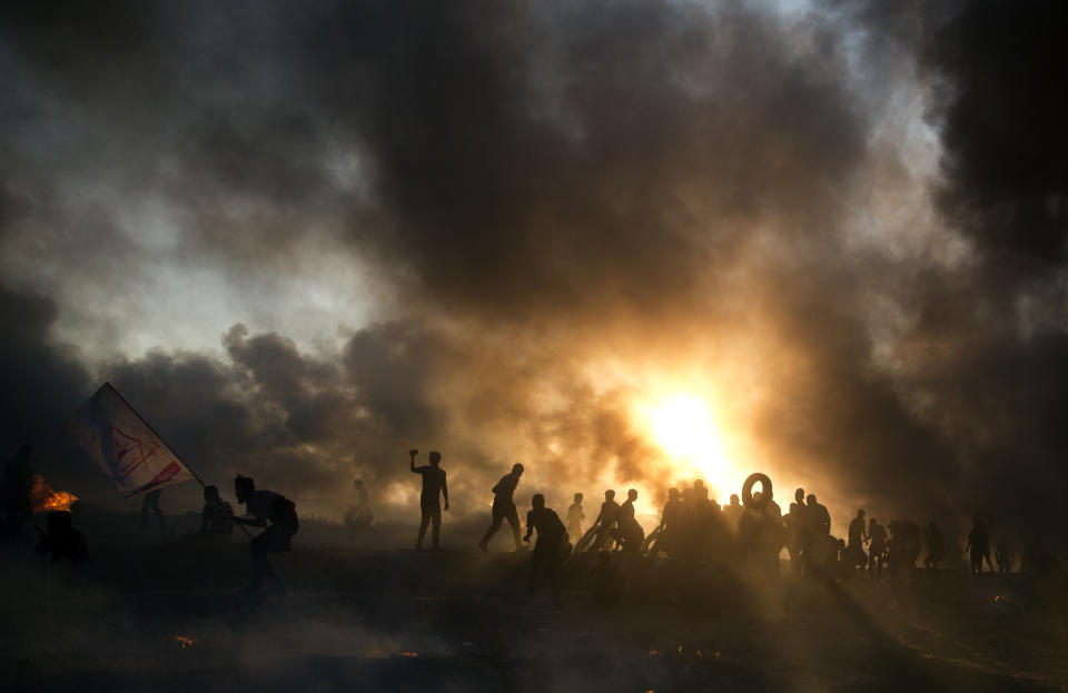 Black smoke from burning tires covers the sky over Palestinian protesters hurl stones toward Israeli troops during a protest at the Gaza Strip's border with Israel, Friday, Oct. 12, 2018. (AP Photo/Khalil Hamra)