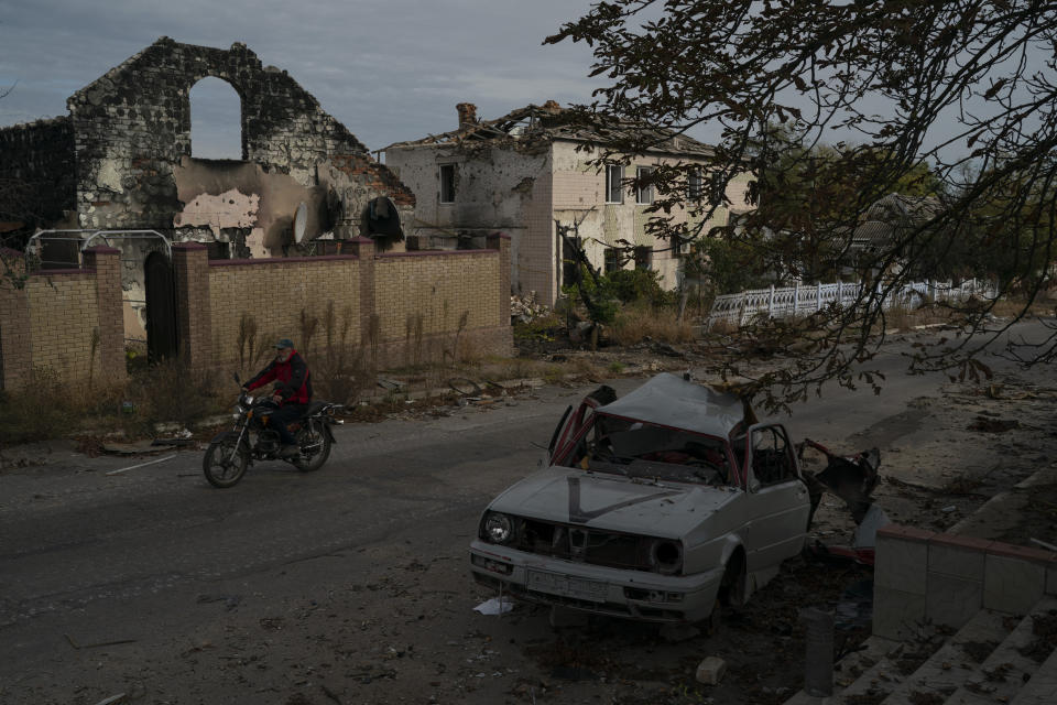 A man drives his motorcycle past a destroyed car in the retaken village of Velyka Oleksandrivka, Ukraine, Wednesday, Oct. 12, 2022. (AP Photo/Leo Correa)