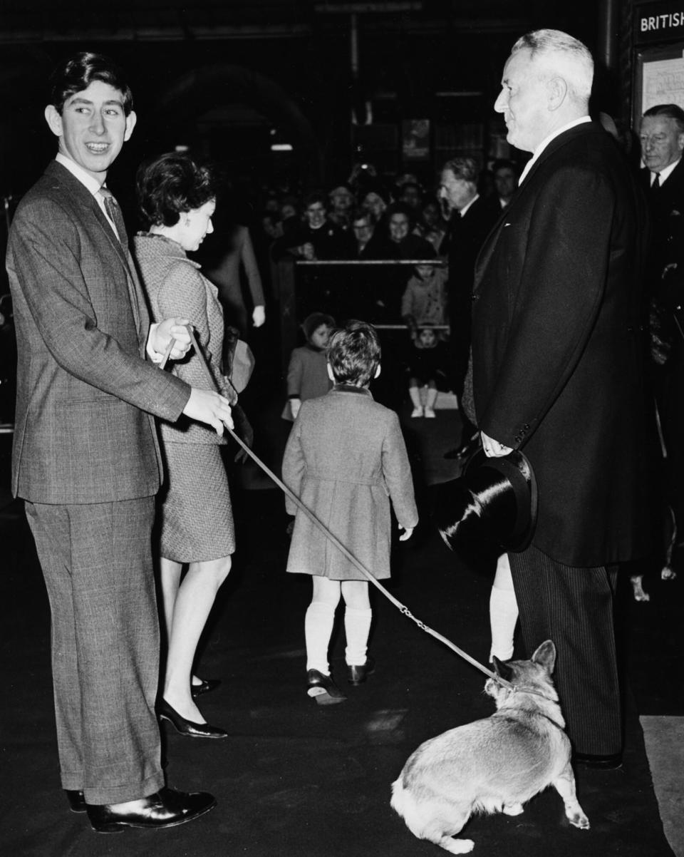 1966, Prince Charles holding a pet corgi on a leash, arriving at Liverpool Street Station, London,