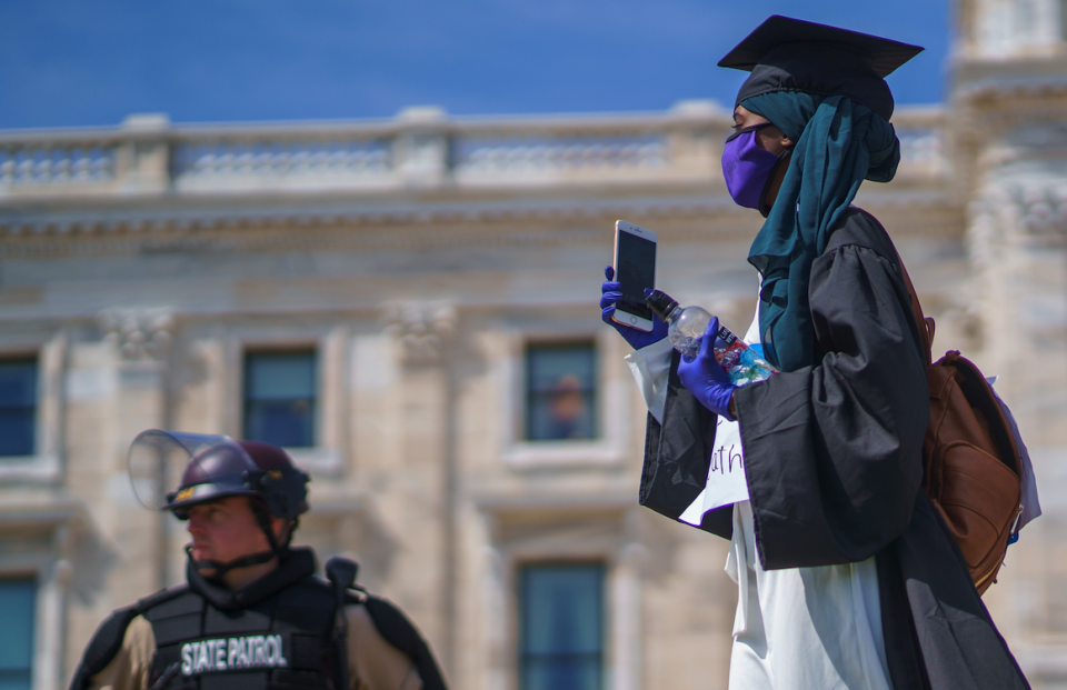 A demonstrator in her graduate outfit walks by Minnesota State Patrol and National Guards standing outside of the state capital building on May 31, 2020 in Saint Paul, Minnesota. (Photo: KEREM YUCEL/AFP via Getty Images) 