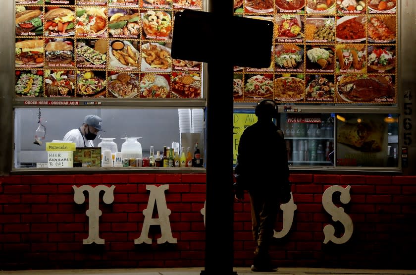 A restaurant worker completes a takeout order for a customer at a taco stand along Redondo Beach Boulevard in Hermosa Beach. Southern California has been in coronavirus lock down for about a month.