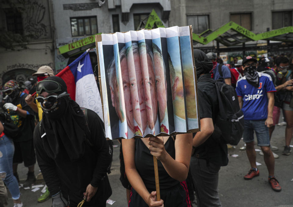 Anti-government protester hold a sign with the portraits of the Chile's President Sebastian Pinera and late military dictator Gen. Augusto Pinochet, during a protest in Santiago, Chile, Monday, Nov. 18, 2019. According to the Medical College of Chile at least 230 people have lost sight after being shot in an eye in the last month while participating in the demonstrations over inequality and better social services. (AP Photo/Esteban Felix)