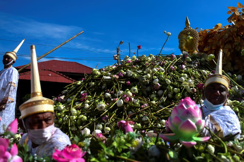 Hombres con máscaras faciales y vestidos con trajes antiguos se sientan junto a una estatua dorada de Buda mientras flota a lo largo de un río, recibiendo flores de los creyentes, durante el festival de la flor de loto, para marcar el final de la cuaresma budista, en Samut Prakan, Tailandia