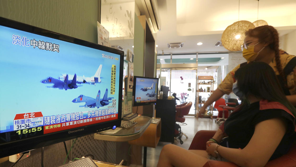 Two people in a beauty salon watch a television showing fighter jets in an apparent Chinese language news report.