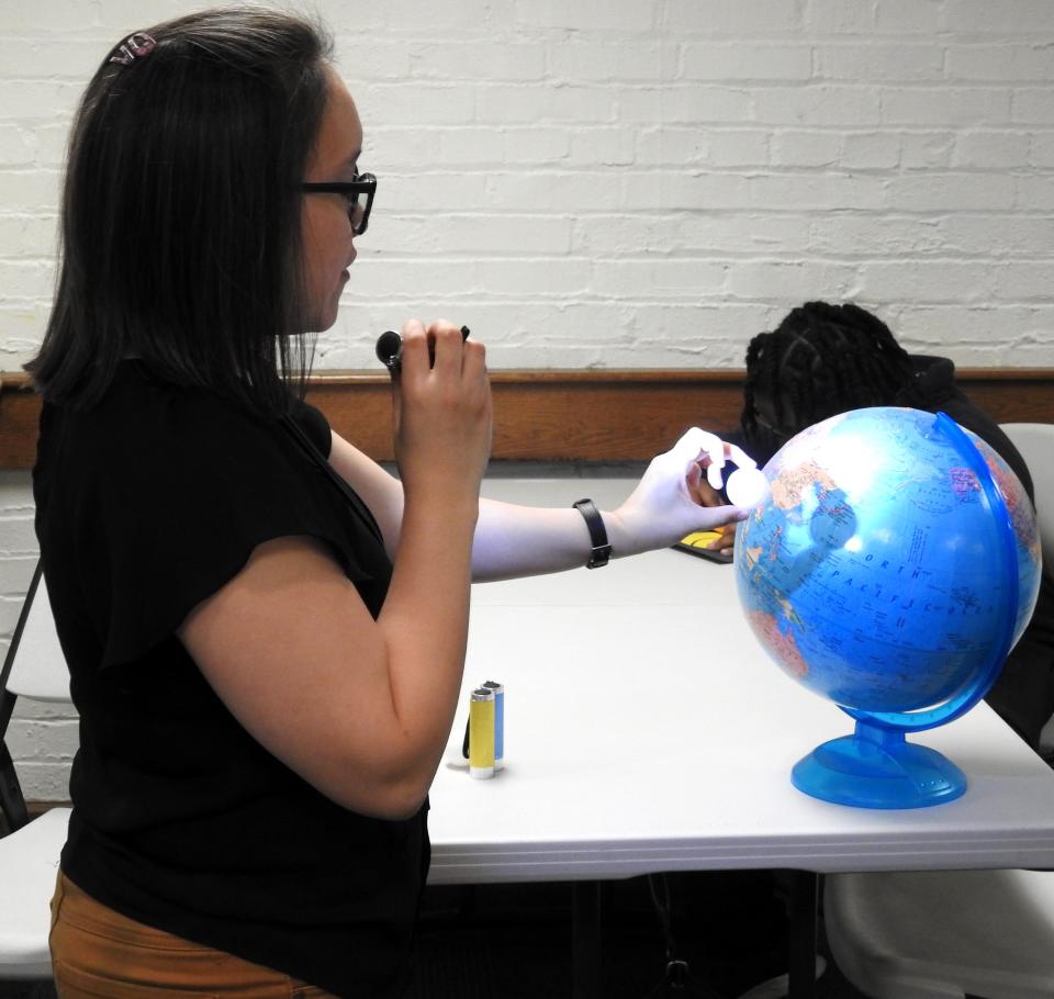 Youth Services Librarian Corazon Britton of the Coshocton County District Library demonstrates the shadow made on the earth during and eclipse to children for a recent youth program. A flashlight shined a light on a ping pong ball positioned between the flashlight and a globe.