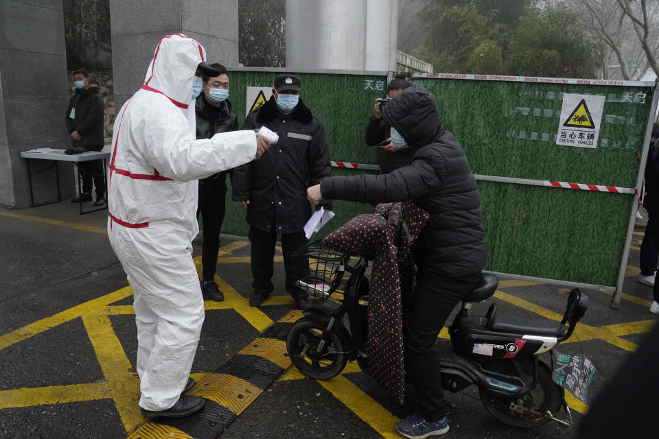 A worker in protective gear checks the temperature of a visitor at the entrance to the Hubei Center for Disease Control and Prevention where a World Health Organization team is making a field visit in Wuhan in central China's Hubei province Monday, Feb. 1, 2021. The WHO mission team investigating the origins of the coronavirus pandemic in Wuhan. (AP Photo/Ng Han Guan)