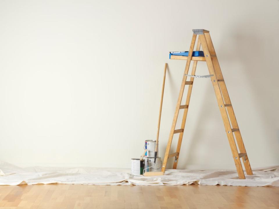 Wood ladder in a home against a blank beige wall, with a dropcloth underneath