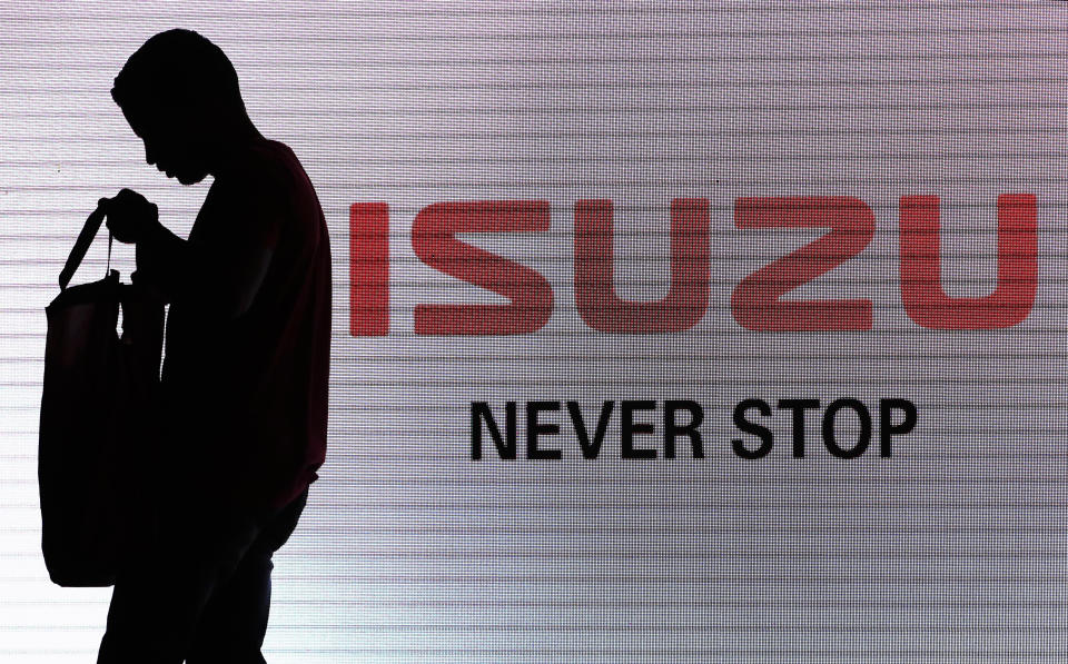 FILE - In this May 11, 2017, file photo, a man walks past the Isuzu logo during the launch of Isuzu MU-X SUV in New Delhi, India. Japanese automakers Toyota, Isuzu and Hino said Wednesday, March 24, 2021 they are setting up a partnership in commercial vehicles to work together in electric, hydrogen, connected and autonomous driving technologies. (AP Photo/Tsering Topgyal, File)