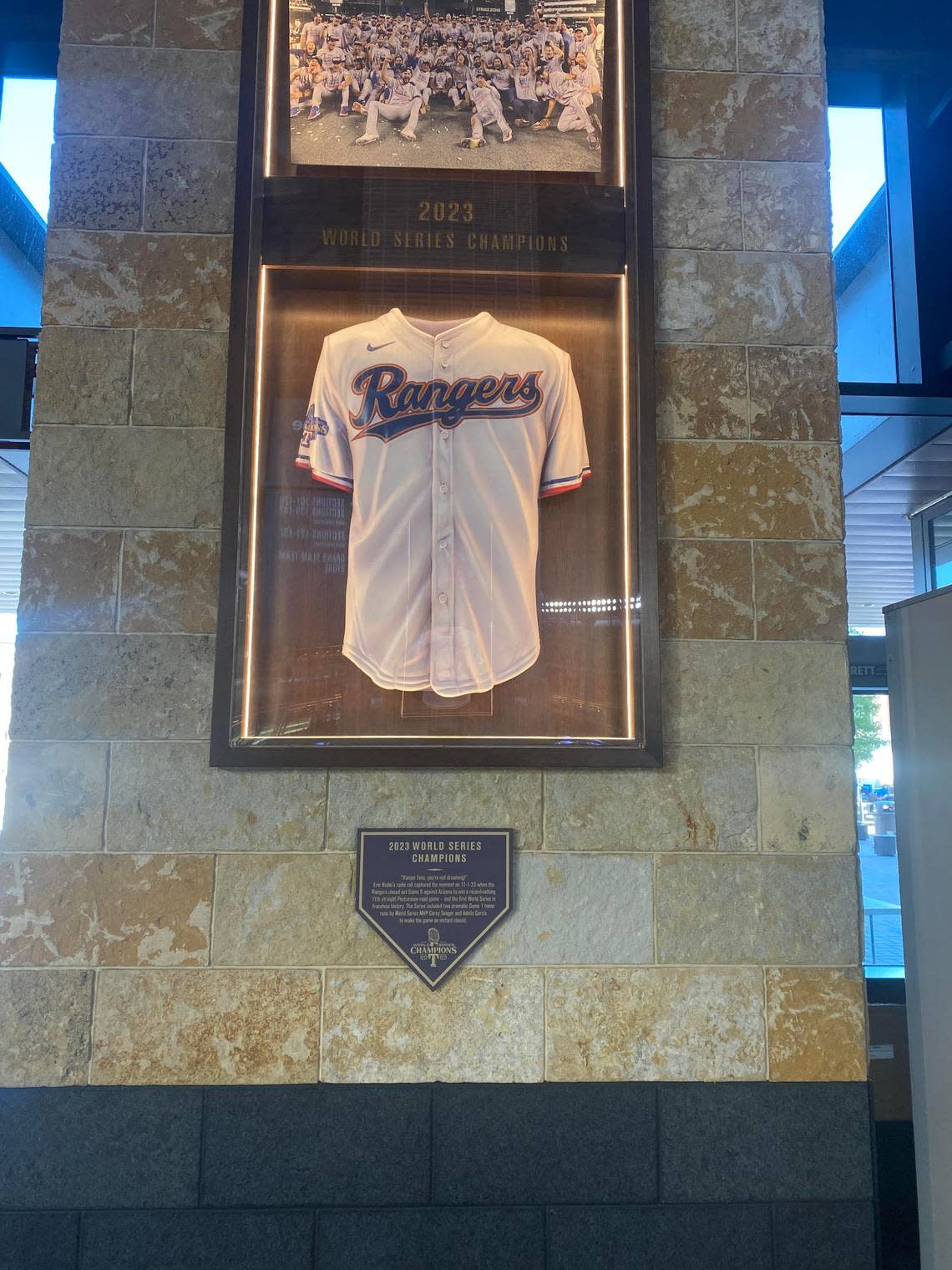 A framed Rangers World Series jersey with a picture o the team after winning the World Series on top of it and a plaque below it. Lawrence Dow