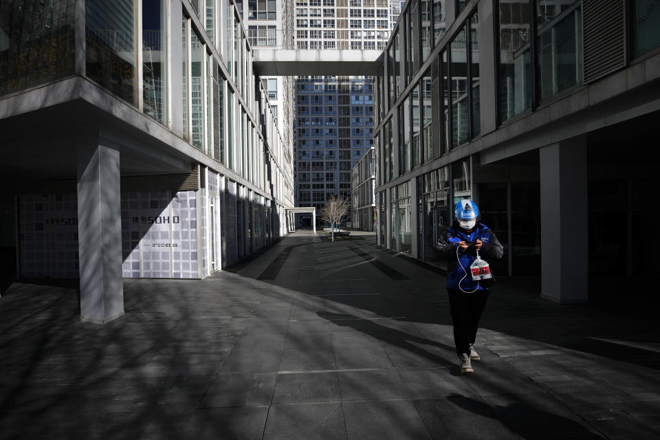 A food delivery worker passes a deserted compound of a commercial office building during the lunch break in Beijing, Monday, Feb. 17, 2020. Chinese authorities on Monday reported a slight upturn in new virus cases and hundred more deaths, as the military dispatched hundreds more medical workers and extra supplies to the city hit hardest by the 2-month-old outbreak. (AP Photo/Andy Wong)