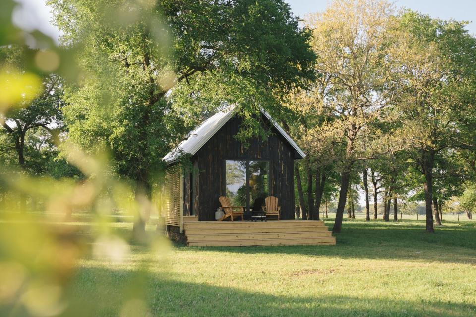 Surrounded by oak trees and lush grasslands, Field Cabin features a steeply pitched roof and an expansive glass door and decking on the front facade.