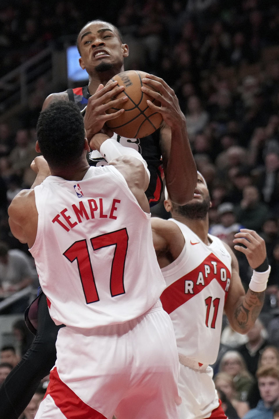 Brooklyn Nets center Nic Claxton, top, vies for control of the ball with Toronto Raptors forward Garrett Temple (17) and Bruce Brown (11) during the second half of an NBA basketball game in Toronto, Monday, March 25, 2024. (Nathan Denette/The Canadian Press via AP)