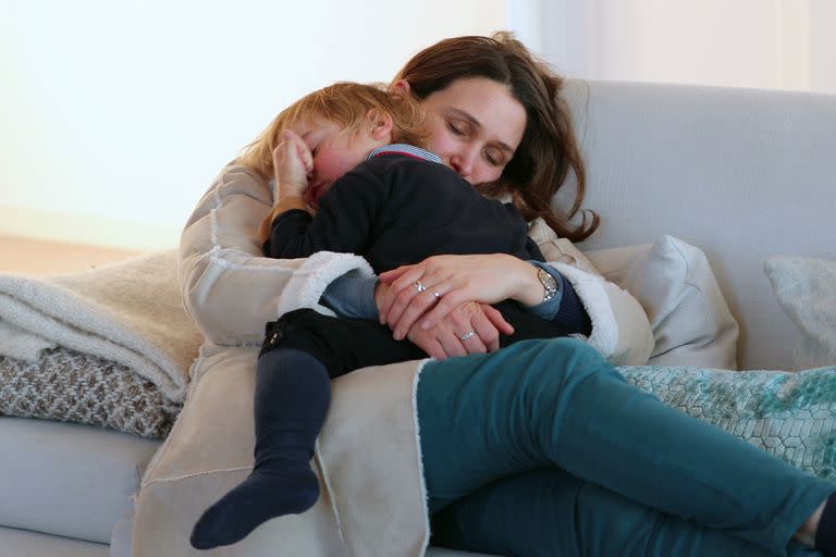 Mom holding her toddler son in her arms. Mother and child falling asleep together in the living room sofa