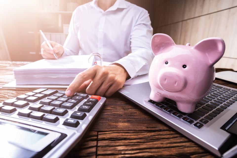 A person using a calculator with a piggy bank in the foreground.