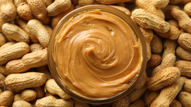Peanut butter in a bowl surrounded by peanuts