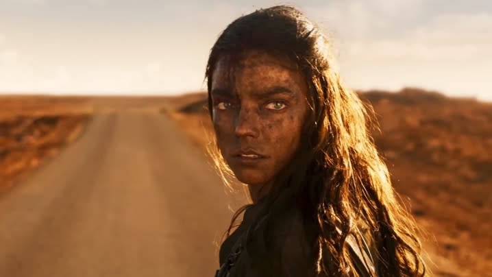 Anya Taylor-Joy stands on a dusty road and glances over her shoulder in a still from "Furiosa: A Mad Max Saga."