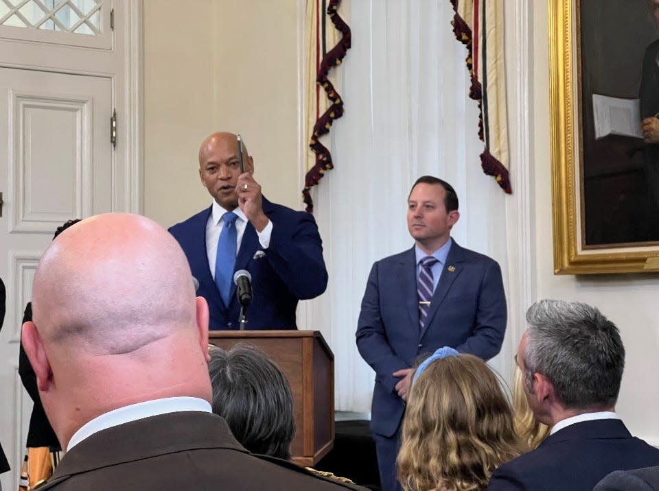 Maryland Gov. Wes Moore, at lectern, presents a pen to Baltimore City Sheriff Sam Cogen, in foreground left, for legislation Cogen supported aimed to reduce evictions in the state in Annapolis on April 25, 2024. Housing Secretary Jake Day, in foreground right, looks on.