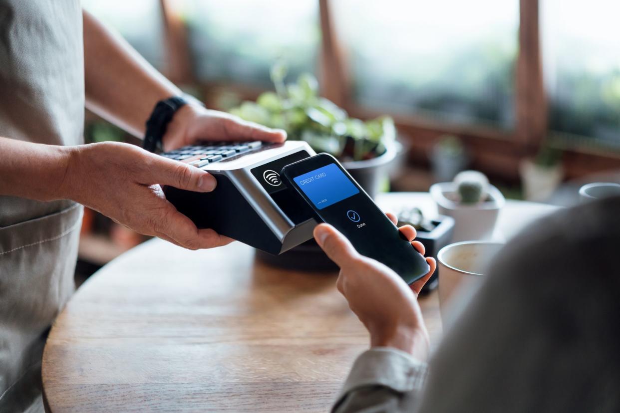 Close up of a male's hand paying bill with credit card contactless payment on smartphone in a cafe, scanning on a card machine. Electronic payment. Banking and technology