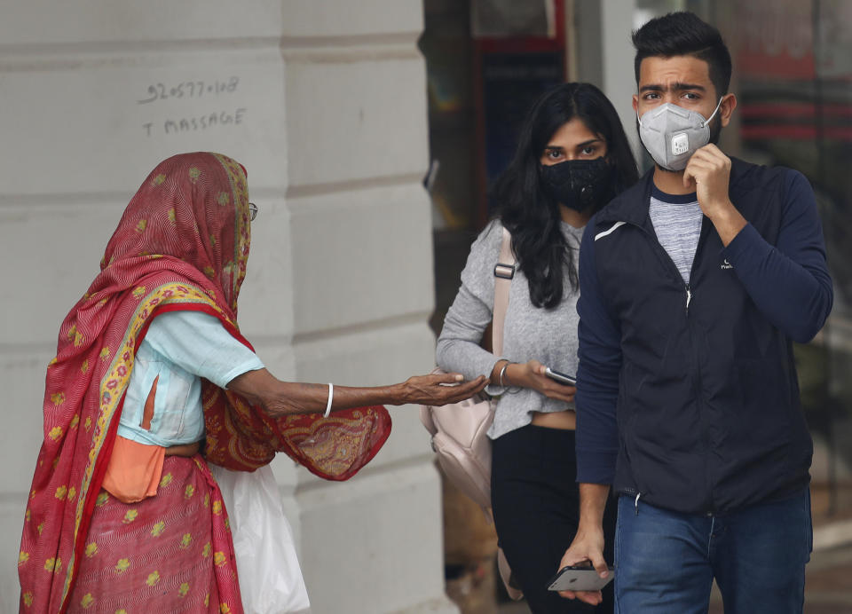 An elderly woman begs as a couple walks wearing pollution mask in New Delhi, India, Thursday, Nov. 14, 2019. Schools in India's capital have been shut for Thursday and Friday after air quality plunged to a severe category for the third consecutive day, enveloping New Delhi in a thick gray haze of noxious air. (AP Photo/Manish Swarup)