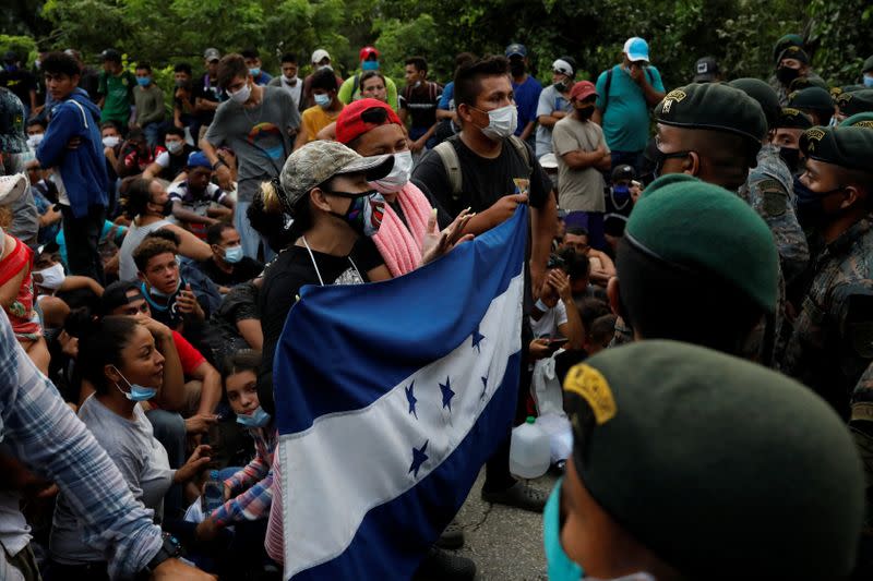 Honduran migrants trying to reach the U.S. hold a Honduran flag while standing in front of Guatemalan soldiers blocking a road to stop migrants from reach the Mexico's border, in San Pedro Cadenas