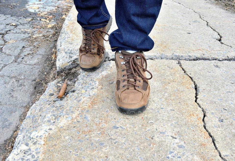 A low angle close up shot, showing a dangerous and neglected sidewalk, even showing a steel support rod protruding through the concrete.