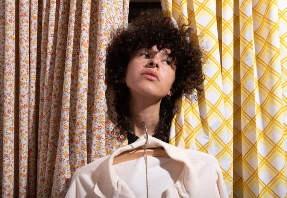 A person with curly hair pokes their head through curtains