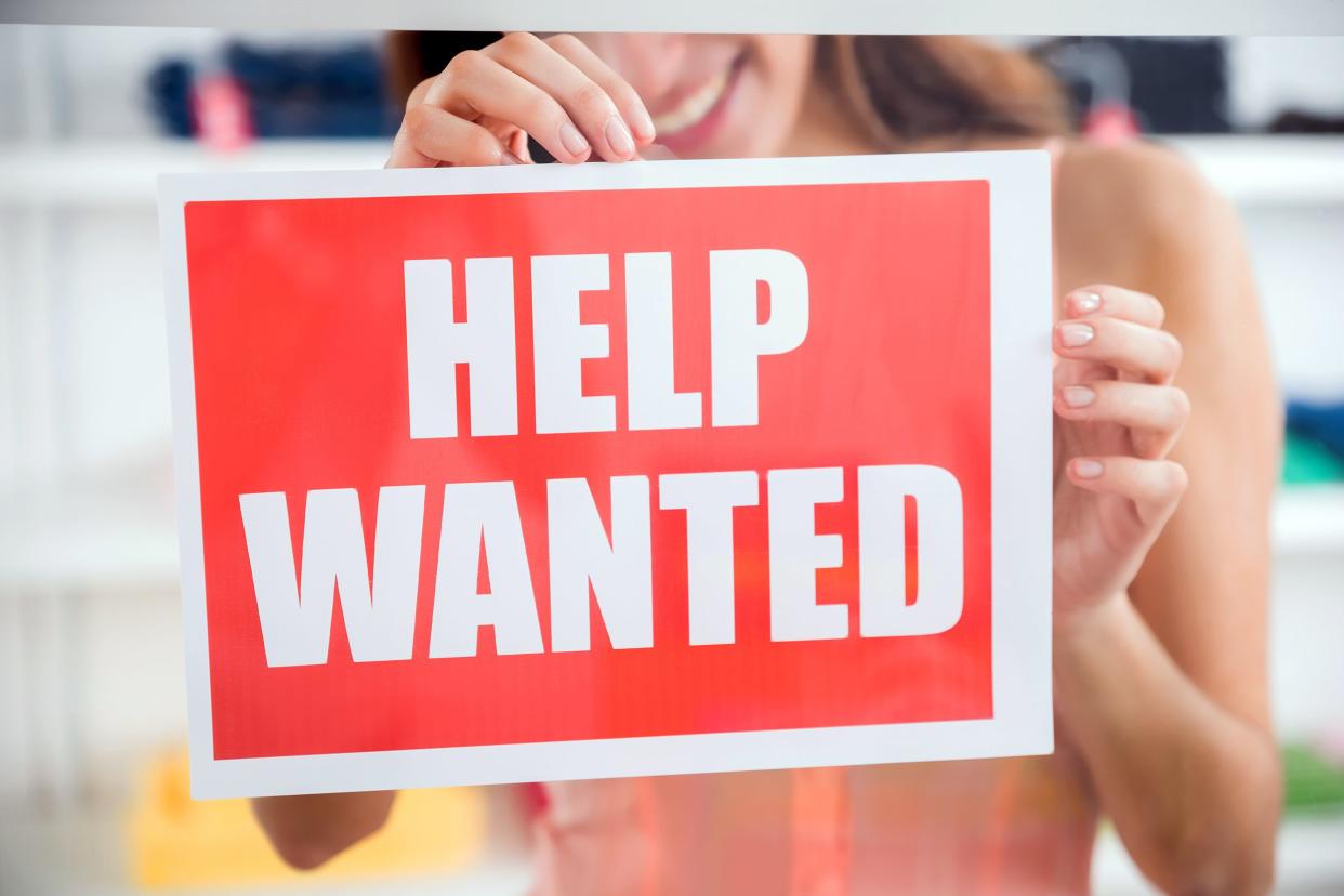 woman hanging 'Help Wanted' sign in store window