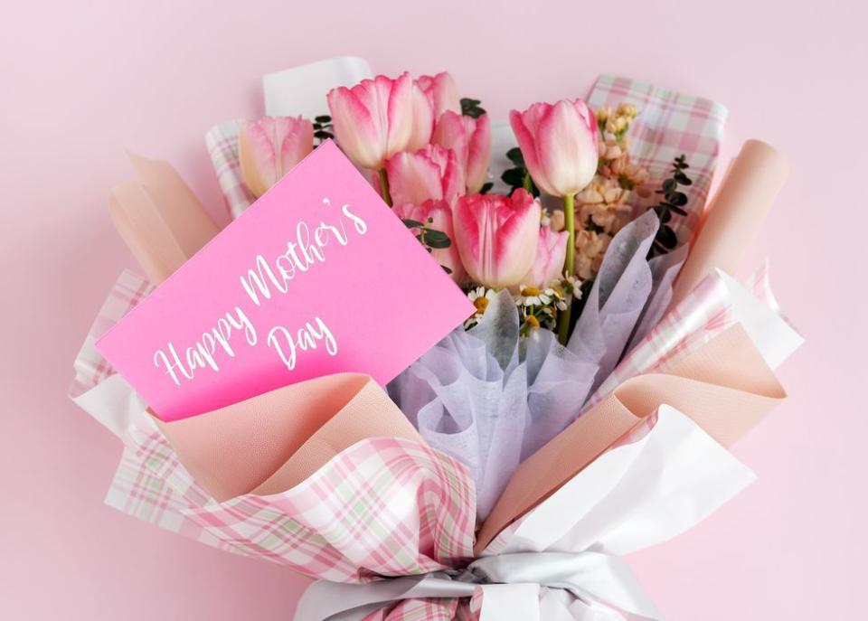 happy mother's day message on a card tucked into a tulip bouquet wrapped in pastel and plaid tissue paper