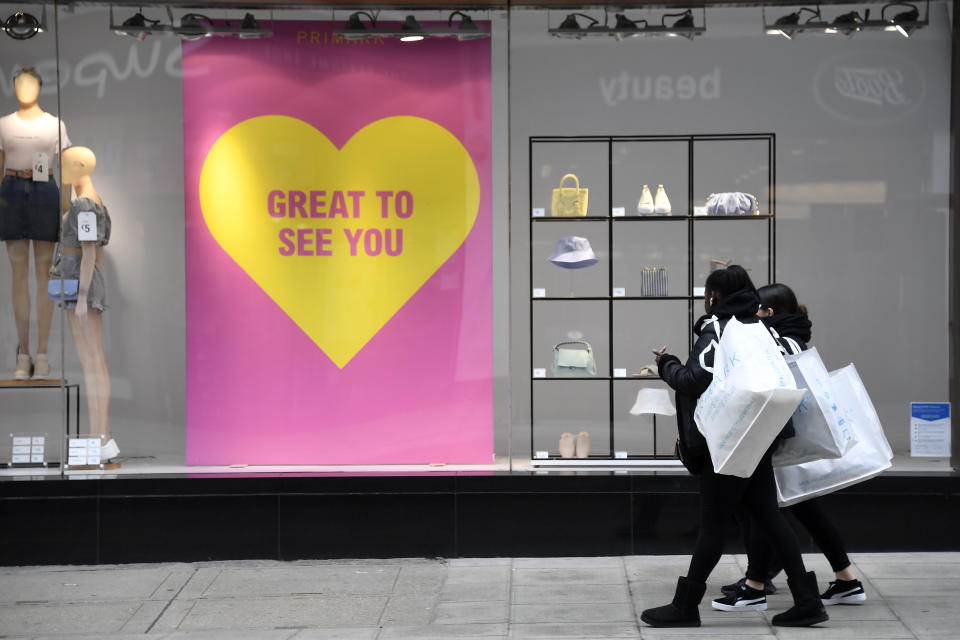 Women carrying shopping bags walk past a shop window in Oxford street in London, Monday, April 12, 2021. Millions of people in England will get their first chance in months for haircuts, casual shopping and restaurant meals on Monday, as the government takes the next step on its lockdown-lifting road map. (AP Photo/Alberto Pezzali)