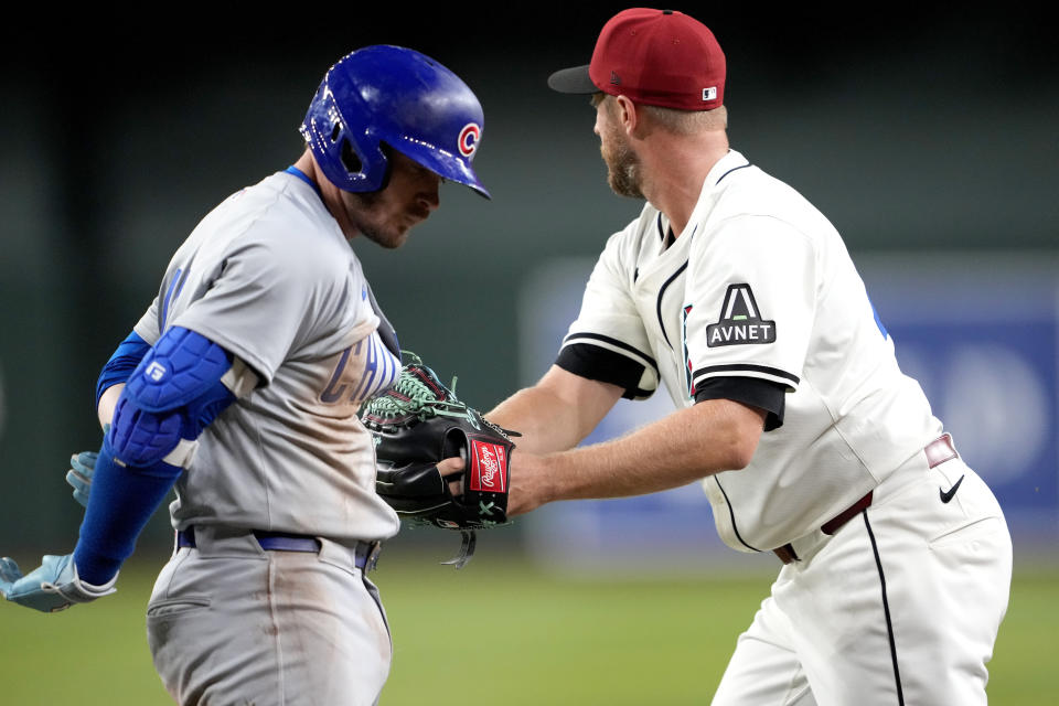 Chicago Cubs' Ian Happ, left, is tagged out by Arizona Diamondbacks pitcher Merrill Kelly on a ground out during the fifth inning of a baseball game, Monday, April 15, 2024, in Phoenix. (AP Photo/Matt York)