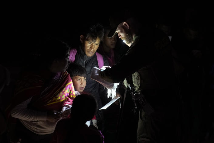 Migrants show their documents to a Border Patrol officer as they are processed after crossing the border Friday, Jan. 6, 2023, near Yuma, Arizona. The Biden administration on Thursday launched an online appointment system for migrants to be exempt from limits on seeking asylum, its latest major step in eight days to overhaul border enforcement. (AP Photo/Gregory Bull)