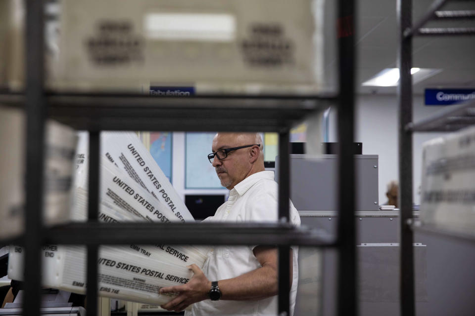 An election worker holds a stack of U.S. Postal Service trays containing mail-in ballots.